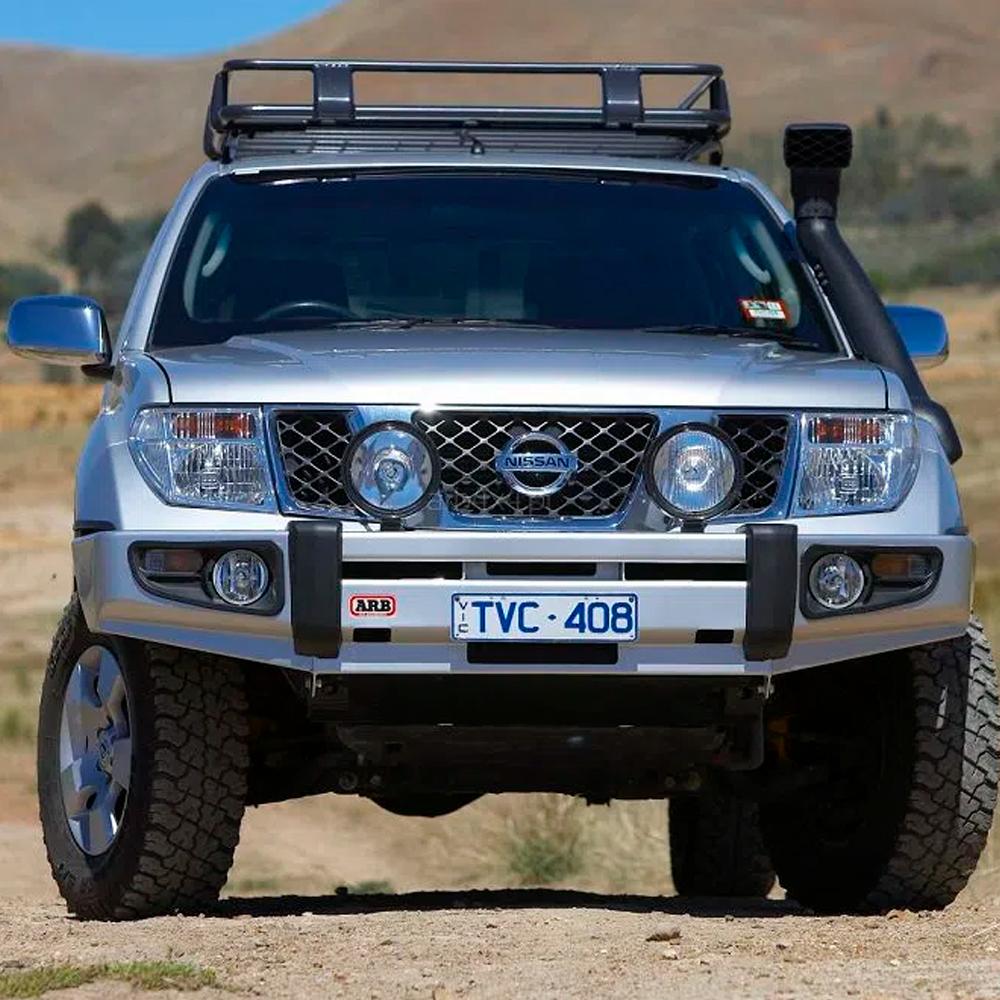 A silver Nissan Navara with secure storage and ARB steel roof racks is parked on a dirt road.