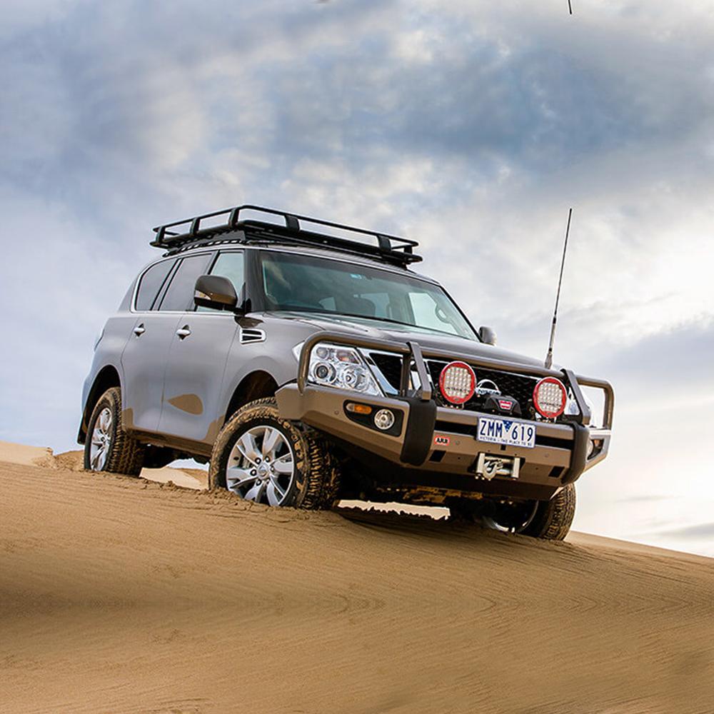 A gray suv with a ARB Roof Rack Mounting Kit for NISSAN and Toyota Land Cruiser ARB 3700100 driving through a sand dune.