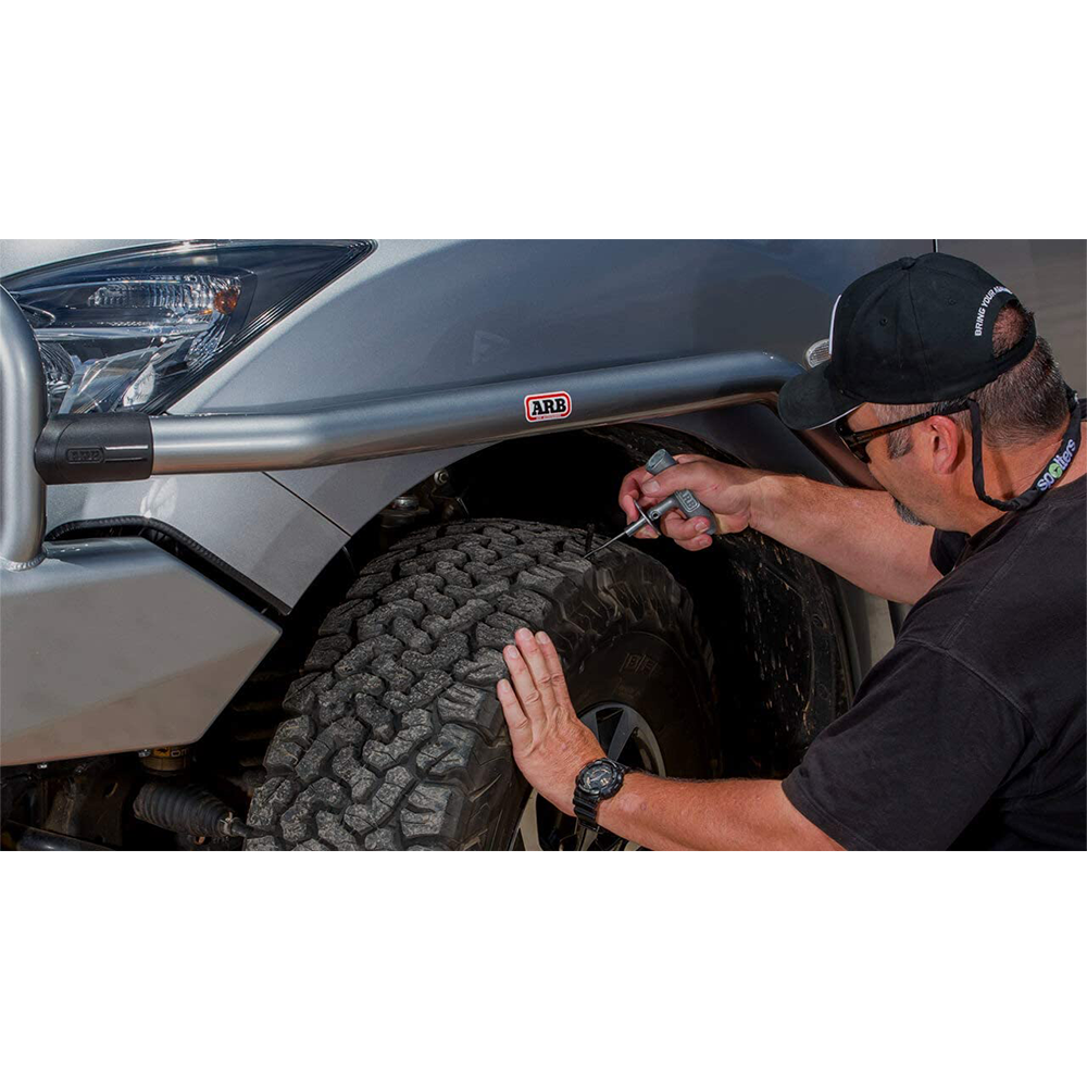 A man is using an ARB Speedy Seal Tire Repair Kit Series II 10000011 to repair a tire on a truck.
