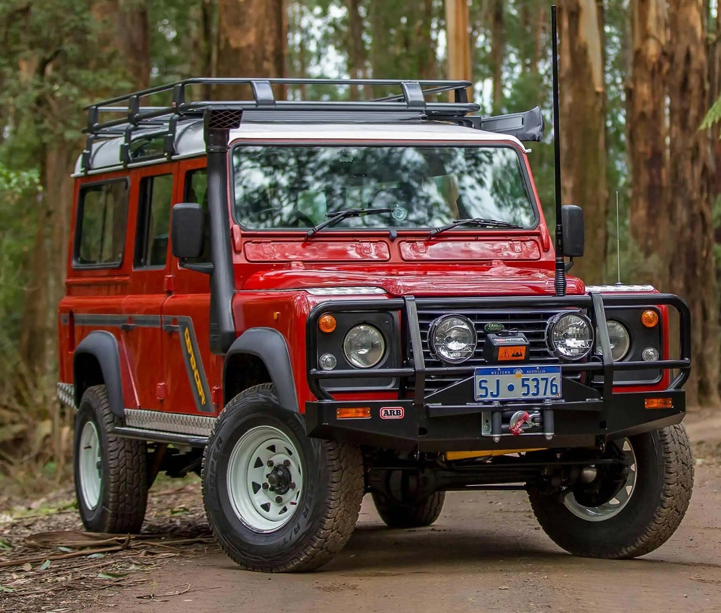 A red Land Rover with Old Man Emu Rear Coil Springs 2755 for Land Rover Defender 110 (1985-2017) is driving down a dirt road, showcasing its easy installation and optimal ride height.