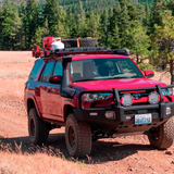 A red ARB 17921030 Base Rack Mount Kit (Black) For Toyota 4Runner (2010-2022) equipped with a roof rack is driving down a dirt road.