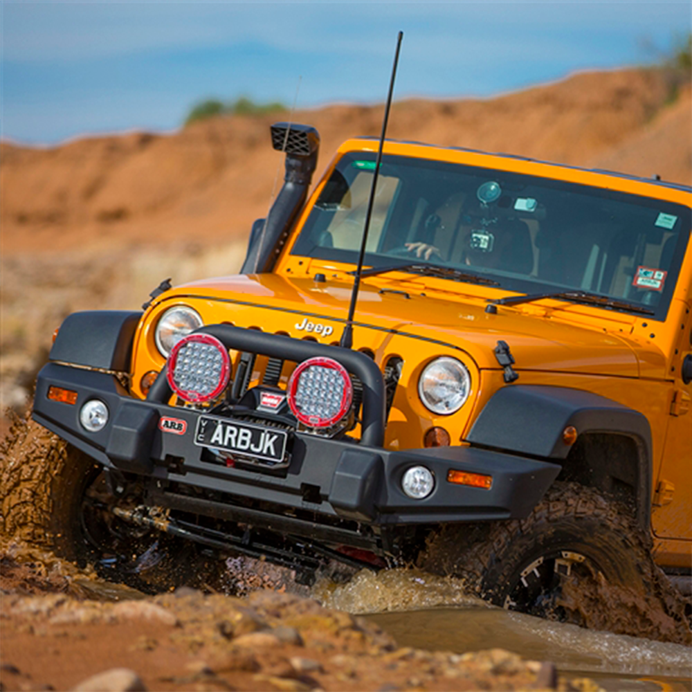 An Old Man Emu jeep with high ride height is driving through a muddy area.