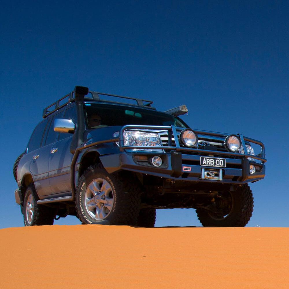 A high capacity ARB Roof Rack Fitting Kit 3713010 (87”x49”) for Toyota Landcruiser 100/105 Series and Lexus Lx470 parked on a sand dune, equipped with secure storage.