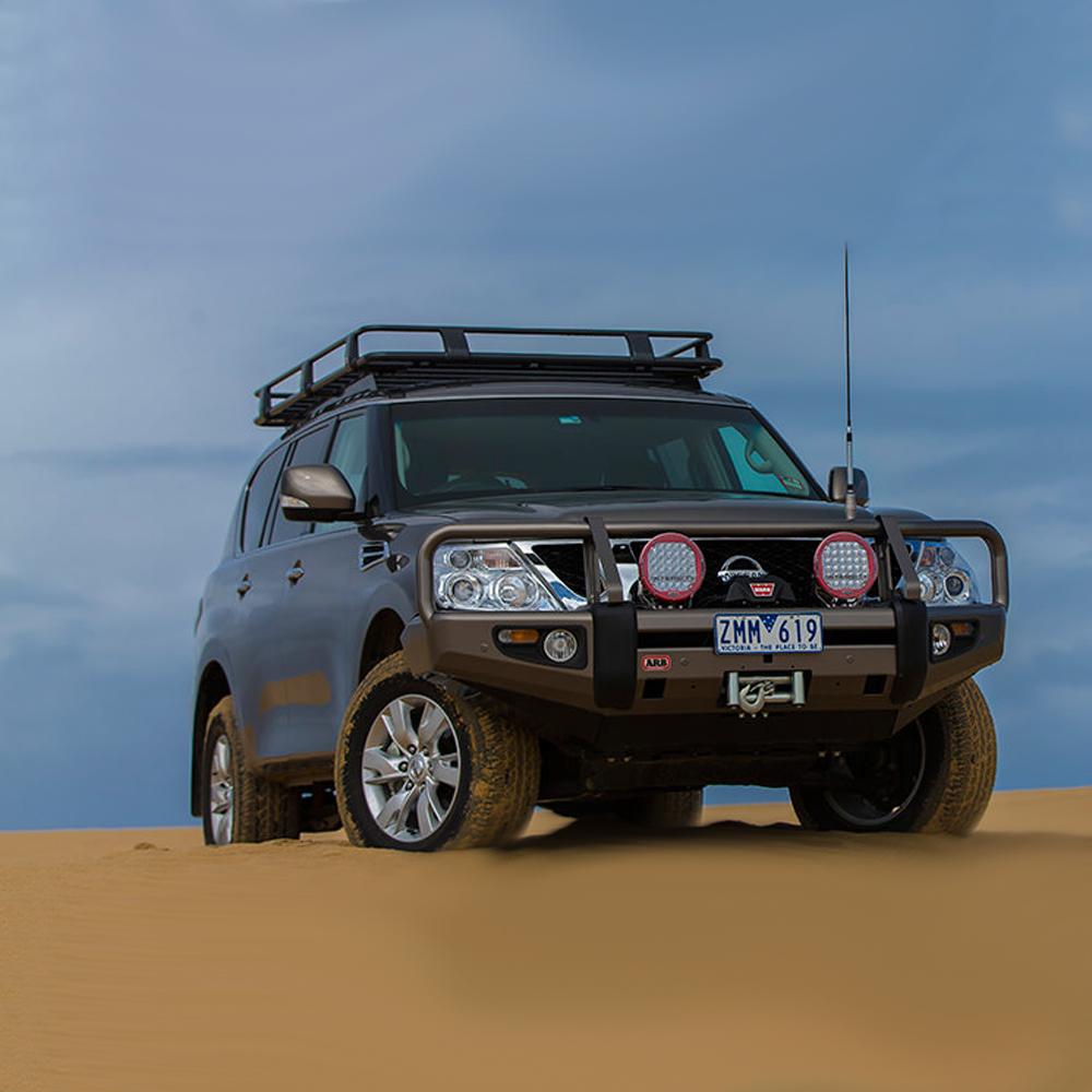 A Nissan Patrol with an ARB stainless steel roof rack securely fitted with an ARB Roof Rack Mounting Kit for NISSAN and Toyota Land Cruiser ARB 3700100, parked in the sand.
