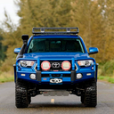 A blue ARB Toyota Tacoma with fog lights is driving down the road.