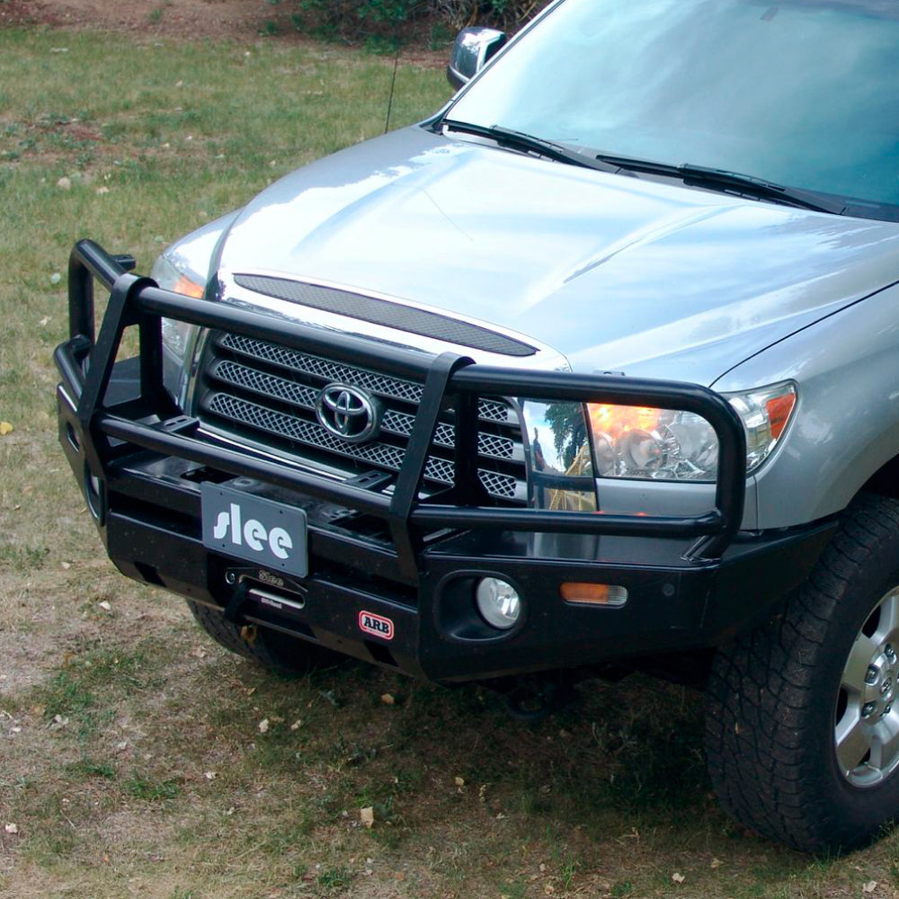 A durable silver Toyota Tundra parked in a grassy area, featuring ARB's Deluxe Bull Bar Winch Bumper For Toyota Tundra 2007-2013 ARB 3415010.