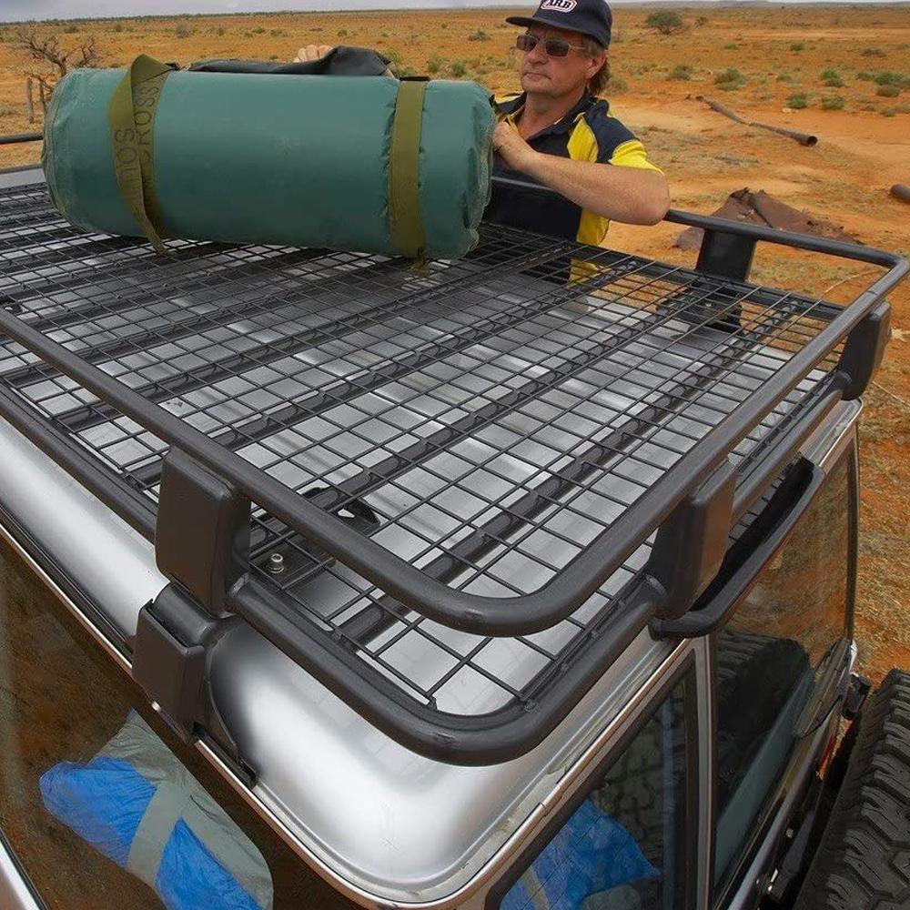 A man with an ARB Steel Rack with Mesh Floor Kit 70” X 44” for Toyota 4Runner 2003-2009 on the roof racks of a jeep, showcasing its high-quality materials and impressive load capacity.