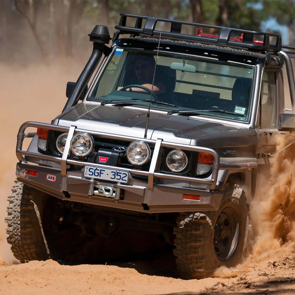 A Toyota Land Cruiser equipped with an ARB Steel Roof Rack Basket with Mesh Floor driving through a dusty area while showcasing its secure storage capabilities.