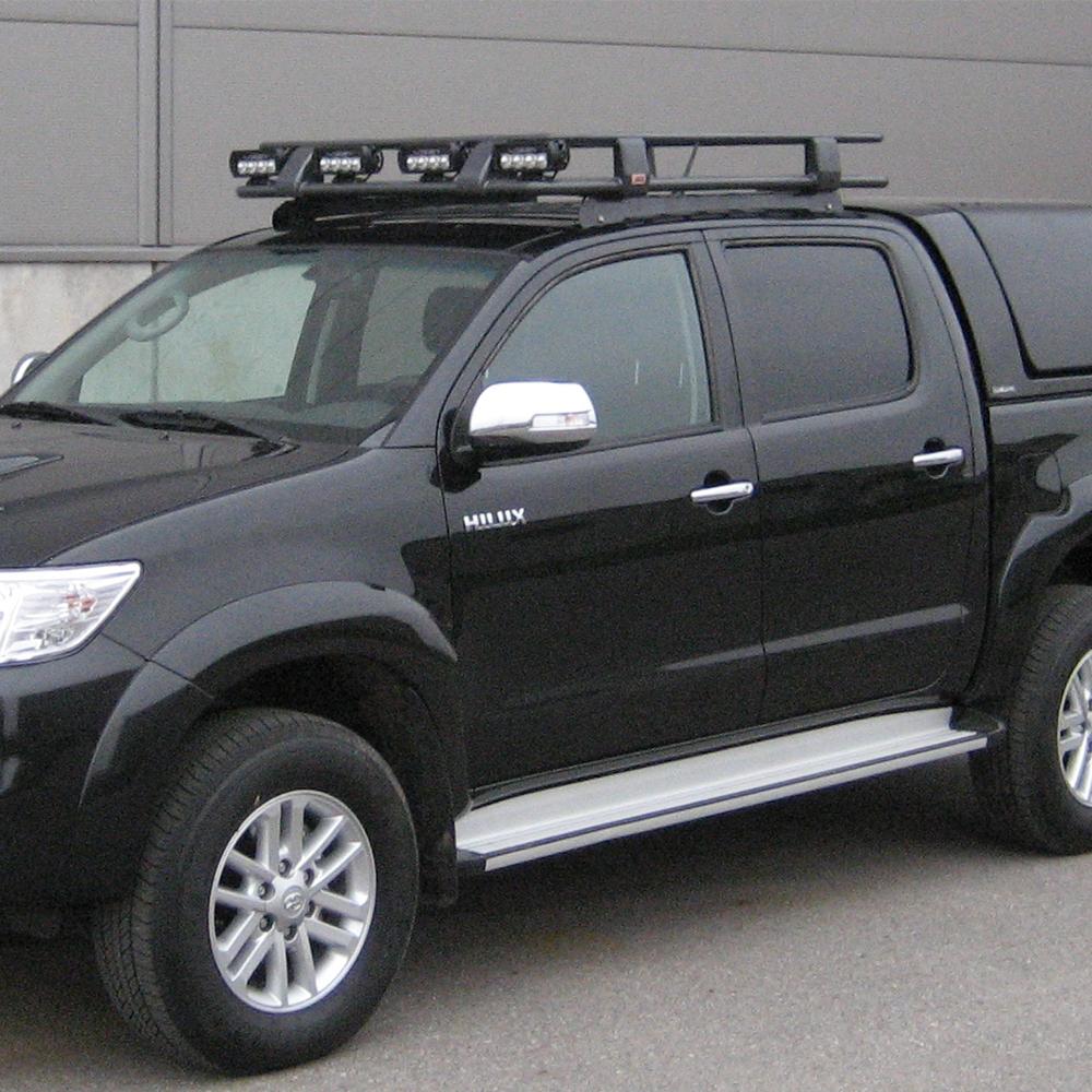 A high capacity black Toyota Hilux, equipped with a Roof Rack Fitting Kit for Toyota Hilux DCab 1997-2011 ARB 3714010 from the brand ARB, parked in front of a building.