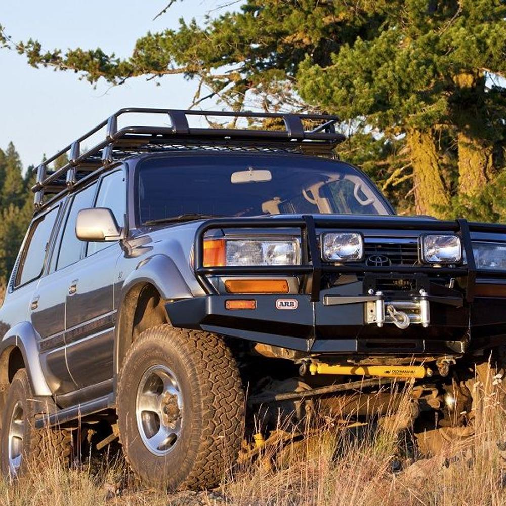 A Toyota Land Cruiser is parked securely on the side of a hill, utilizing an ARB Steel Rack with Mesh Floor 43” X 49" for Jeep Cherokee XJ ARB 3800030MK fitting kit for added stability.