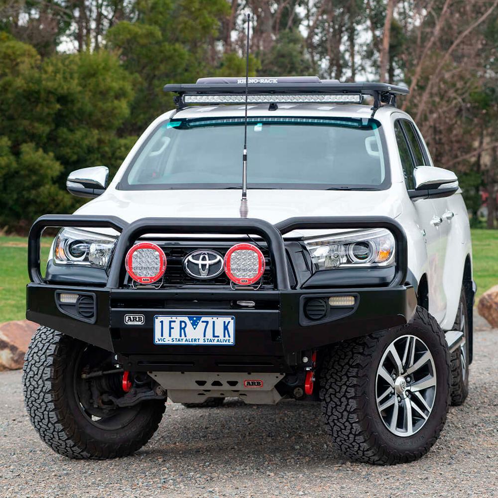A white ARB Alloy Flat Rack 70” X 44” with Mesh Floor for Toyota Land Cruiser 100 Series 1997-2007 parked on a gravel road, offering secure storage.