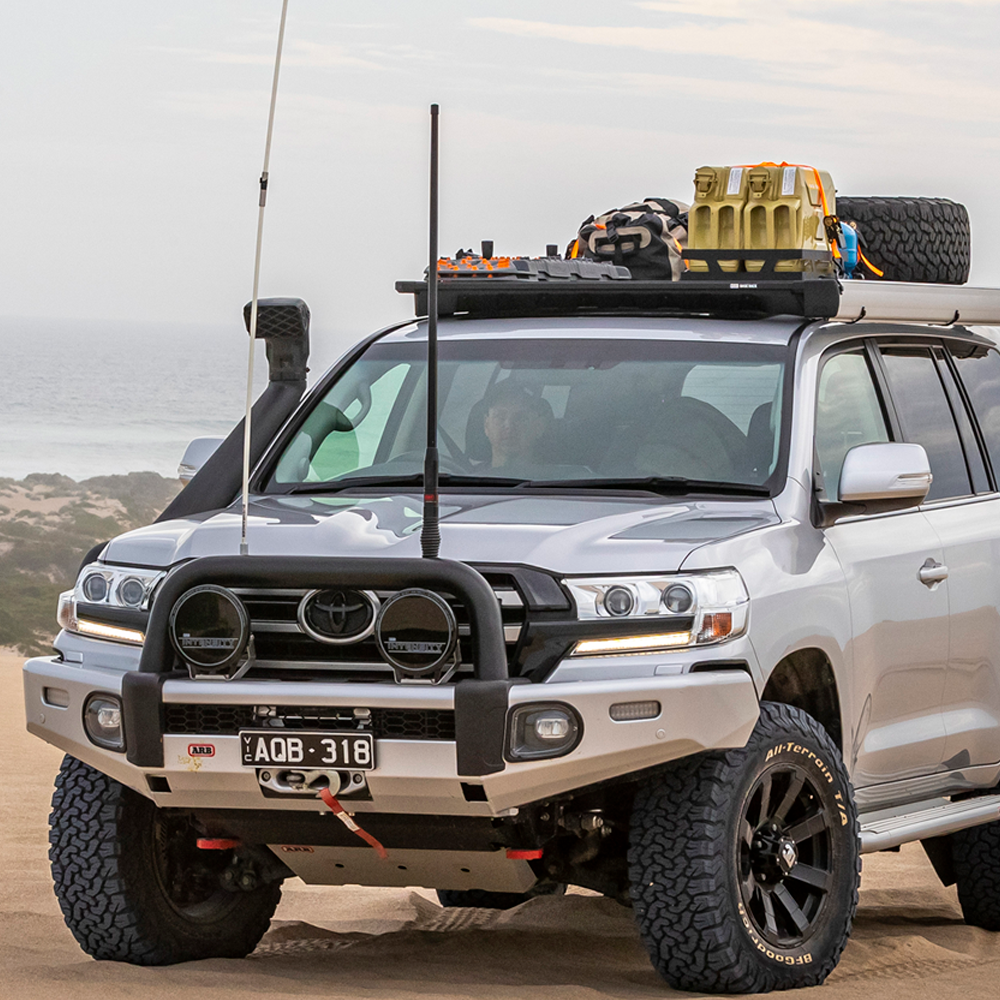A silver ARB Toyota Land Cruiser with an Alloy Flat Rack With Mesh Floor for Toyota Land Cruiser 200 Series ARB 4900040MKLC2 is parked in the sand, providing maximum protection and displaying an impressive approach angle.