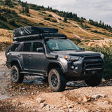 The Old Man Emu Rear Coil Springs 2895 for Toyota Prado 150 & 120 Series, 4Runner, FJ Cruiser, Hilux, known for their impressive ride height and off-roading capabilities, are securely parked in a rocky area.