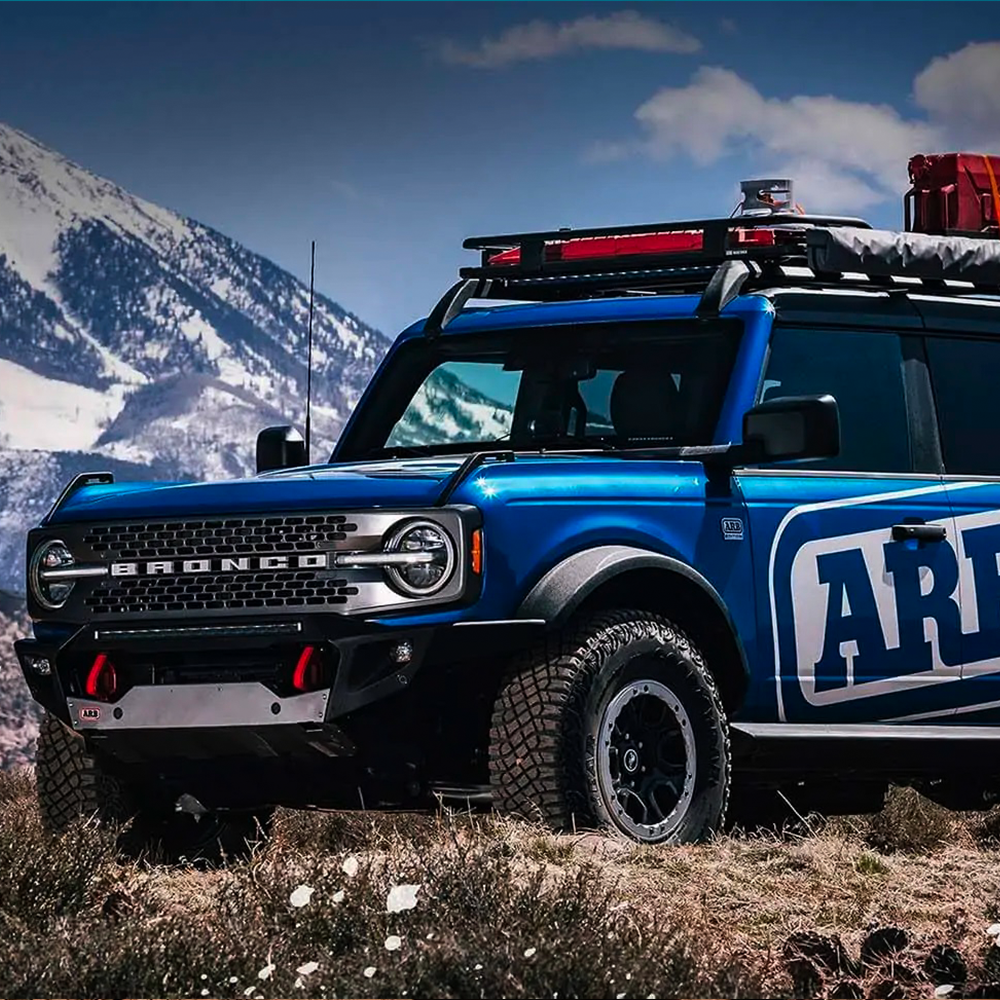 A blue Ford Bronco, equipped with an Old Man Emu Front Stabilizer Bar Kit OMESTAB10 by Old Man Emu for enhanced ride quality, is parked on the side of a mountain.