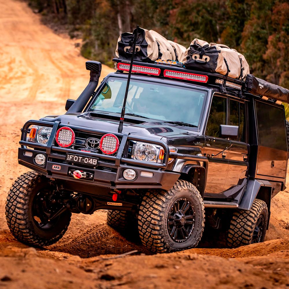 A black Old Man Emu Toyota Land Cruiser equipped with an ARB Old Man Emu Rear Nitrocharger Sport 60081 for Prado 150 Series LWB (Coil Spring Models Only) driving down a dirt road.