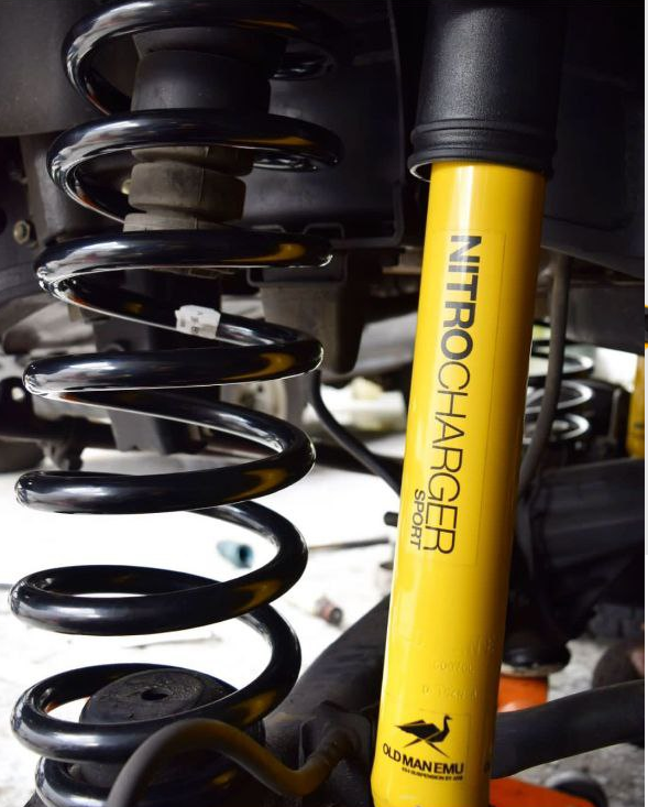 The suspension of a vehicle with "Old Man Emu Front Nitrocharger Sport Shock 60000 for Toyota LandCruiser 100 Series (IFS) Not AHC Models" from the brand "Old Man Emu", which includes compression valving and nitrogen gas.