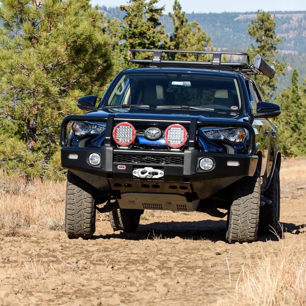 A black Toyota Tacoma equipped with ARB Touring Roof Racks 3813200KJK is driving down a dirt road, demonstrating its carrying capacity.