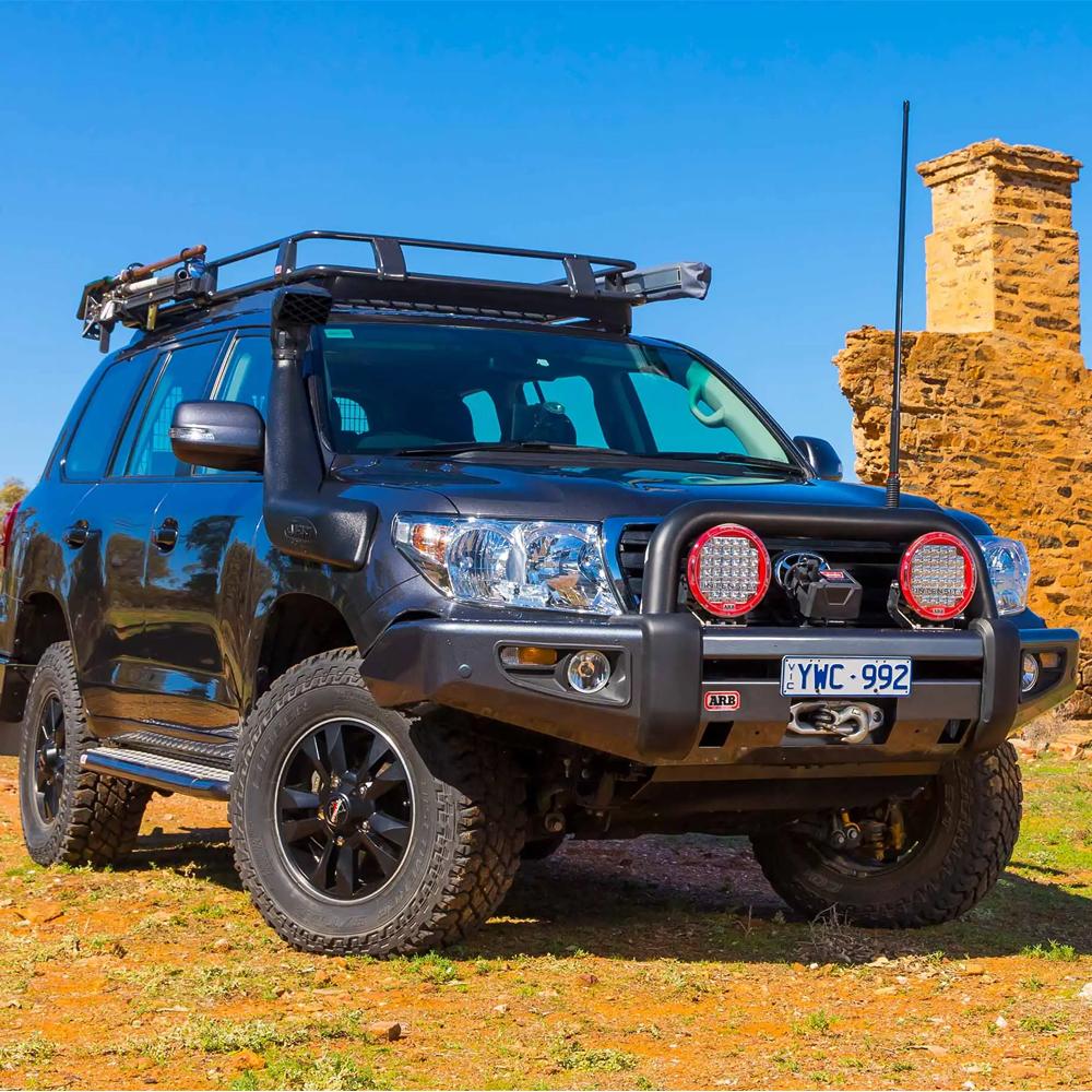 A black ARB Land Cruiser equipped with a Steel Basket Rack Kit 87” X 44” for Land Cruiser 200 Series 2008 - 2021 (ARB 3800040KLC2), parked on a dirt road.