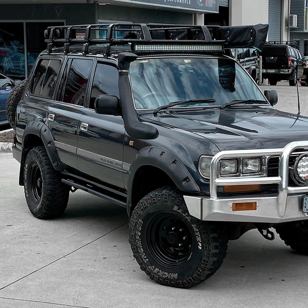 A Toyota Land Cruiser parked in front of a building with a ARB Steel Rack with Mesh Floor 43” X 49" for Jeep Cherokee XJ ARB 3800030MK installed.