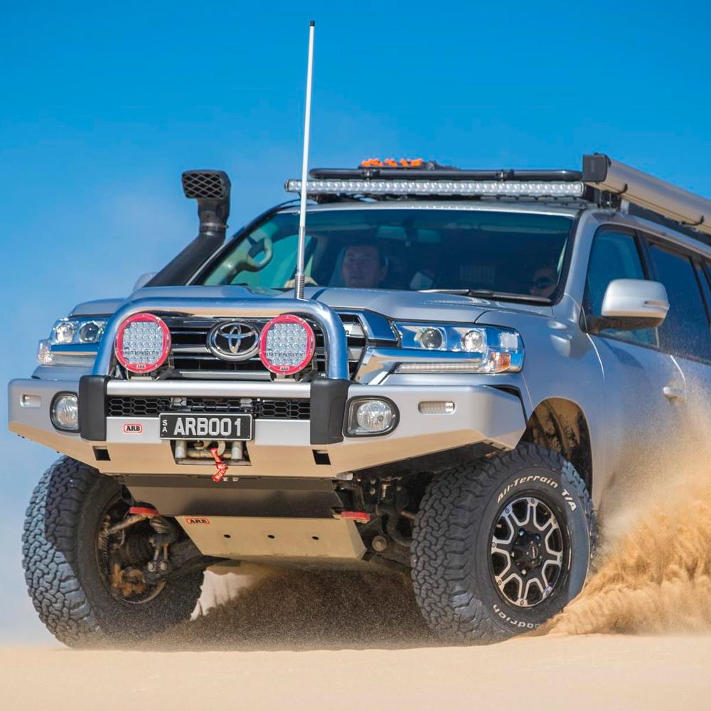 A silver ARB Toyota Land Cruiser equipped with secure storage and an Alloy Flat Rack 87"X49" with Mesh Floor ARB 4900060M fitting kit, driving through the desert.