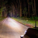 An ARB Intensity Solis Lighting Kit + Wiring Loom (SPOT / FLOOD)  SJB36S / SJB36F / SJBHARN driving down a dimly lit road in the woods.