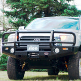 A Toyota Tacoma with durable steel construction parked in a field, featuring an "Deluxe Bull Bar Winch Bumper For Toyota Tundra 2007-2013 ARB 3415010" by ARB.