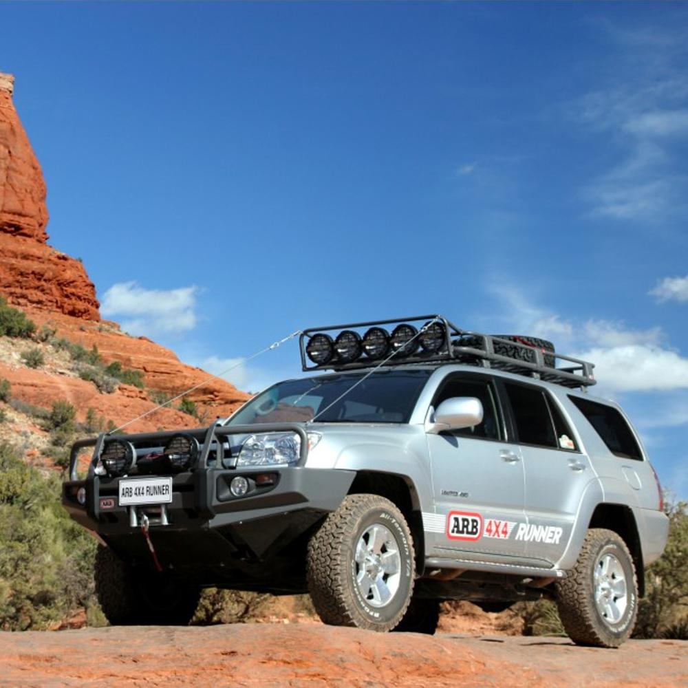 An ARB Alloy Roof Rack Basket 87” X 49” ARB 4900010M is parked in front of a red rock, offering secure storage for outdoor excursions with its fitting kit.