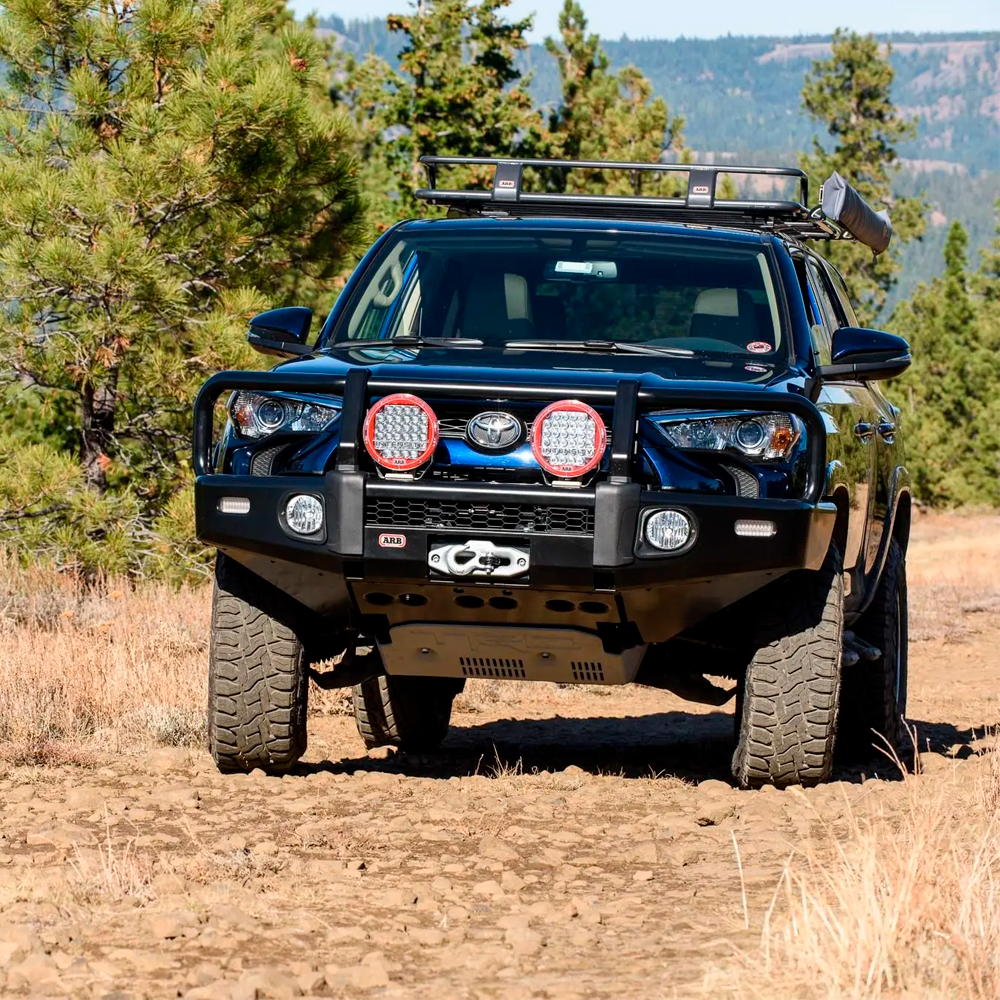 A black Toyota 4Runner with an ARB Touring Roof Rack FJ Cruiser (2007-2009) 3800200KLC2 is driving down a dirt road.