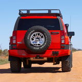 A red jeep with high capacity secure storage on a dirt road, equipped with the Roof Rack Fitting Kit for Hummer H3 2006 from ARB.