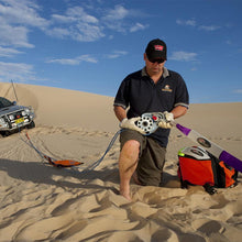 Load image into Gallery viewer, A man kneeling in the sand next to an ARB Snatch Pack Recovery Bag ARB502A.