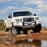 A white Toyota Tacoma is driving through a muddy area with its Old Man Emu Heavy Duty Front Nitrocharger Sport Strut 90010 for effective protection against impacts and high-quality Old Man Emu oil for optimal performance.