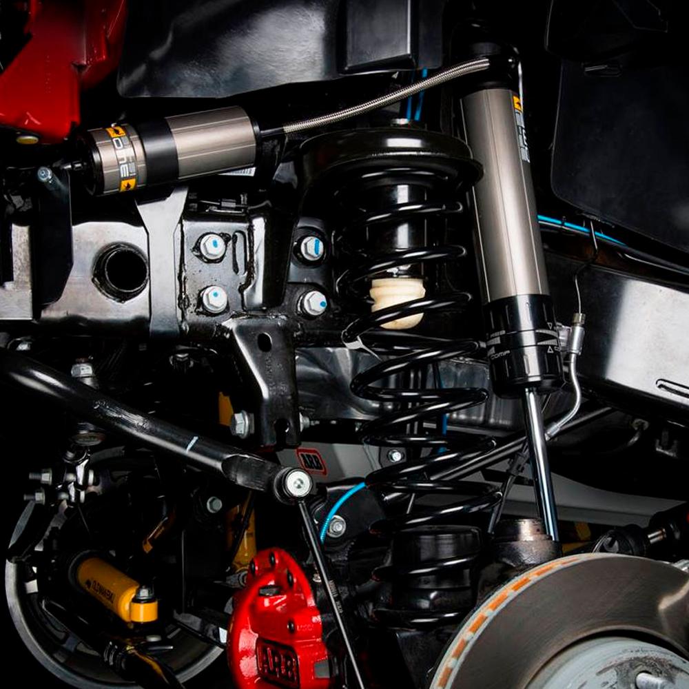 A close up of a motorcycle suspension system featuring an Old Man Emu BP-51 Front Shock Absorber BP5160045 for Land Rover Defender 110 (85-17) with a remote reservoir and high-temperature hose.