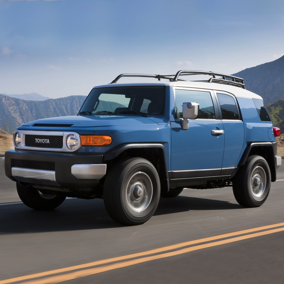 The blue Toyota FJ Cruiser, equipped with the Old Man Emu OME BP-51 2.5 - 3 inch Lift Kit for FJ Cruiser (10-ON) suspension and shock absorbers, is driving down the road.