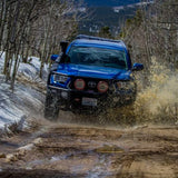 A blue Toyota Tacoma equipped with an Old Man Emu OME BP-51 2-3 inch Lift Kit for Tacoma (05-23) suspension system and shock absorbers is smoothly driving down a dirt road, showcasing its exceptional adjustable damping feature.