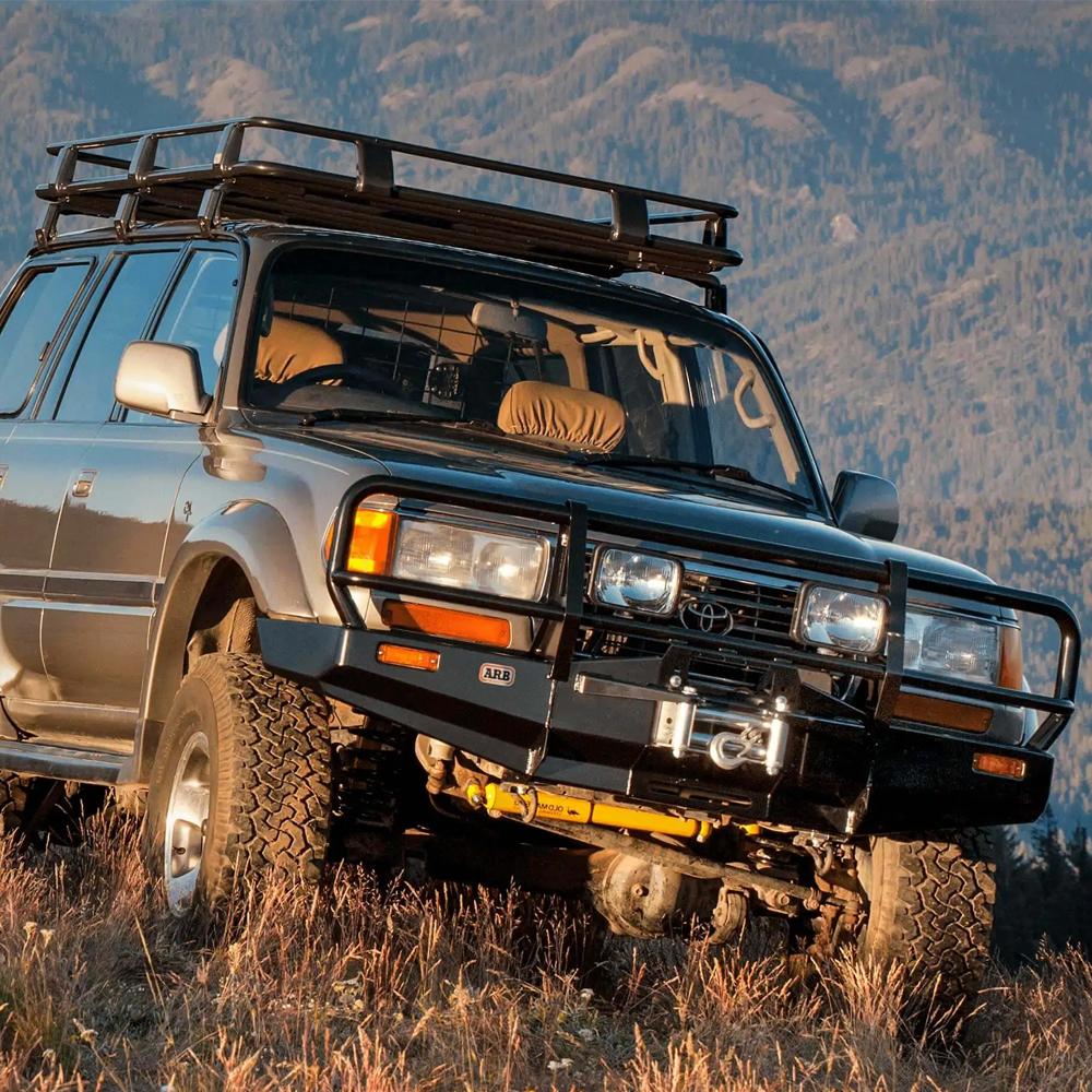 An ARB Steel Rack with Mesh Floor Kit 70” X 44” for Toyota 4Runner 2003-2009 parked in a field with mountains in the background.
