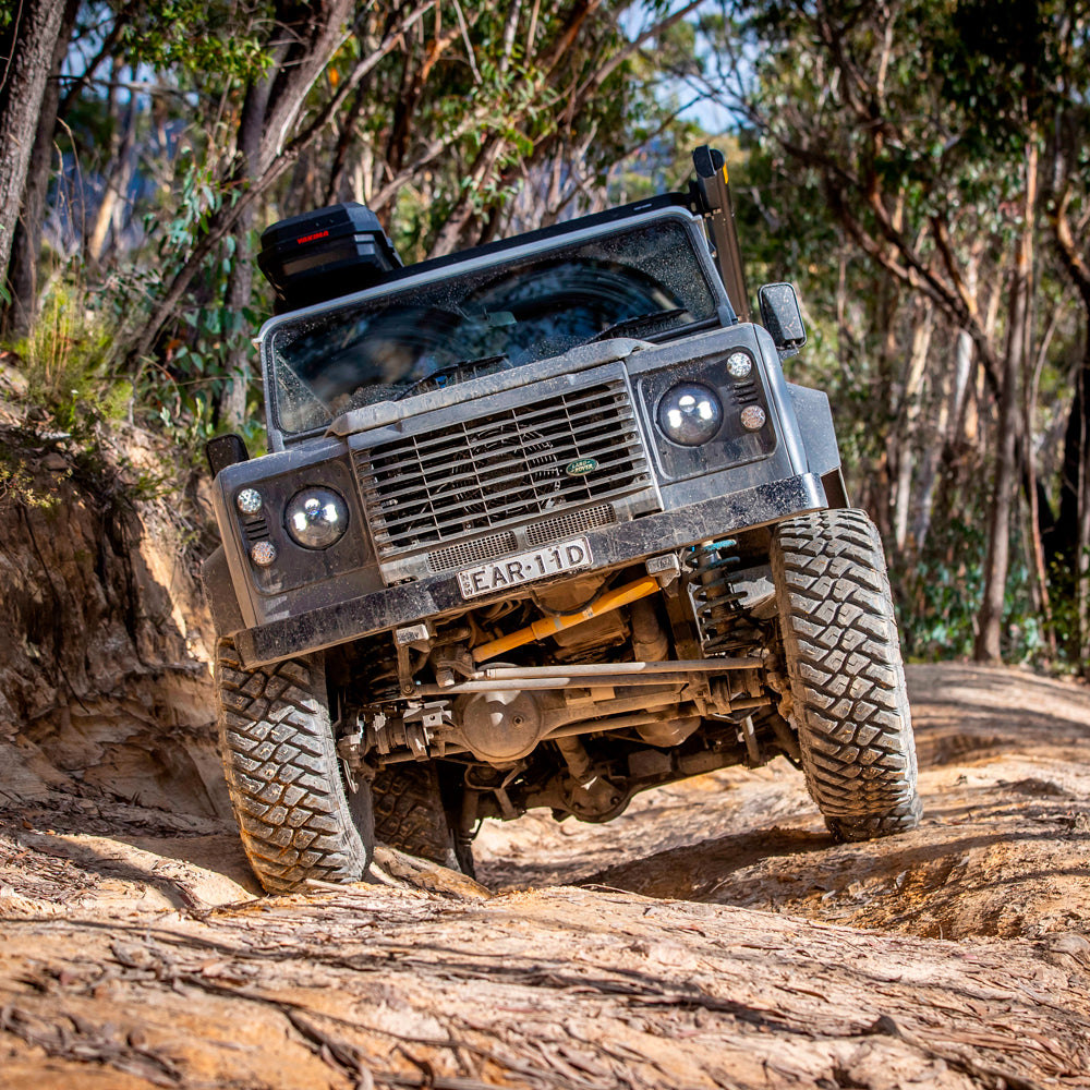An OME 2 inch Lift Kit for Land Rover Defender 110 (85-17)-equipped Old Man Emu land rover is confidently driving down a dirt road, thanks to its exceptional ground clearance and advanced suspension system.