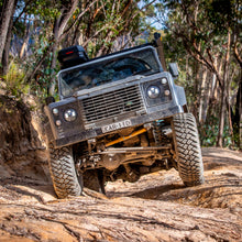 Load image into Gallery viewer, An OME 2 inch Lift Kit for Land Rover Defender 110 (85-17)-equipped Old Man Emu land rover is confidently driving down a dirt road, thanks to its exceptional ground clearance and advanced suspension system.