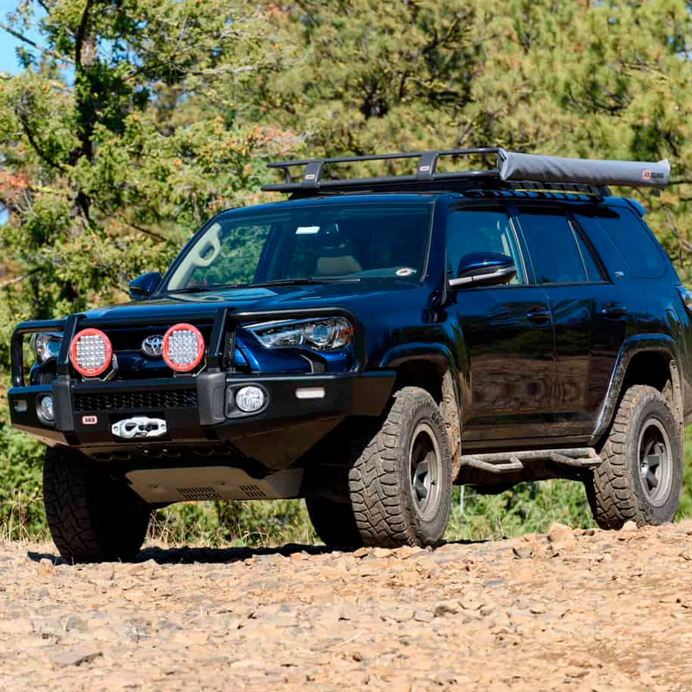 A black Toyota 4Runner with an ARB Touring Roof Rack FJ Cruiser (2007-2009) 3800200KLC2 is parked on a dirt road.