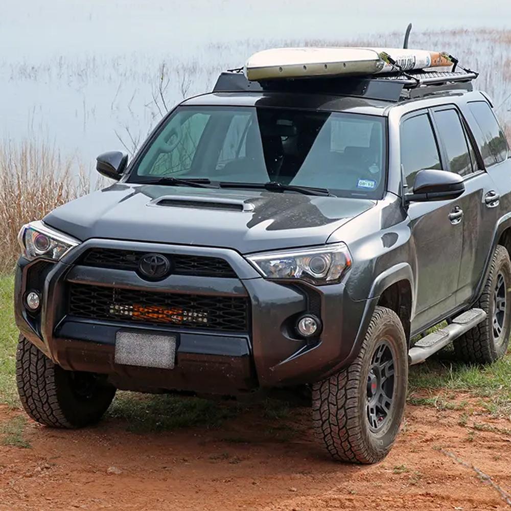 A high capacity gray ARB 4Runner with an ARB Steel Flat Rack 70” X 44” for Toyota 4Runner 2003-2009 (ARB 3813010k4) installed on top, along with a surfboard.