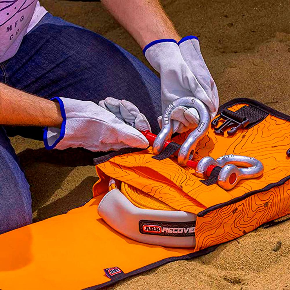 A man is holding a waterproof orange Compact Recovery Bag ARB503A in the sand.