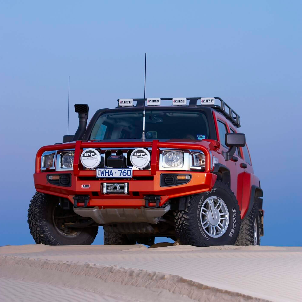 A red SUV with high capacity secure storage Roof Rack Fitting Kit for Hummer H3 2006 ARB 3768010, conquering a sand dune.