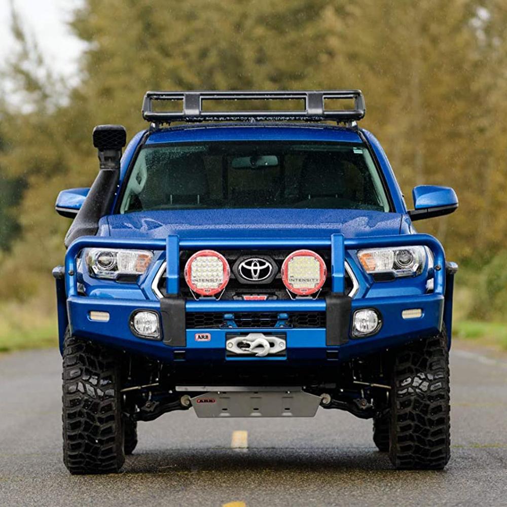 A blue ARB Toyota Tacoma with high capacity is driving down a country road.