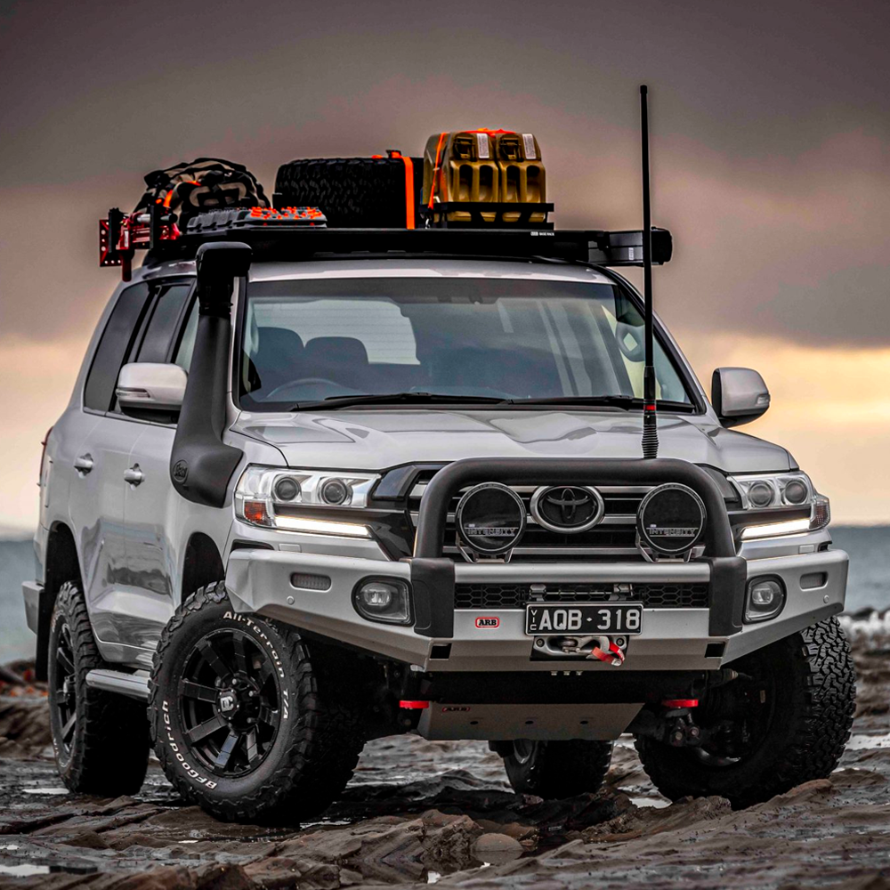 An ARB Alloy Flat Rack With Mesh Floor for Toyota Land Cruiser 200 Series ARB 4900040MKLC2 is parked on a rocky beach, providing maximum protection and showcasing its impressive approach angle.