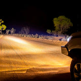 An ARB Intensity Solis Lighting Kit + Wiring Loom (SPOT / FLOOD)  SJB36S / SJB36F / SJBHARN is driving down a dimly lit dirt road at night.