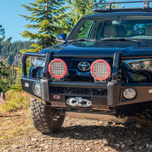 Load image into Gallery viewer, A black Toyota Tacoma, equipped with the ARB Under Vehicle Skid Plates System with kinetic (KDSS) 5421110 from ARB, is parked in a forest.