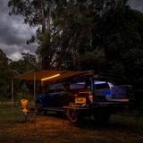 An ARB Touring Awning with Light 814409 truck is parked in a waterproof wooded area at night.