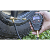 A person is using the ARB E-Z Deflator Digital Gauge ARB510 from ARB Air Systems to measure the tire pressure.