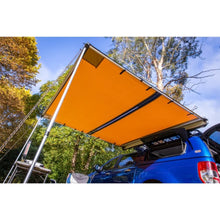 Load image into Gallery viewer, A blue car with an ARB Touring Awning with Light 814410 attached to its roof racks.