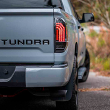 Load image into Gallery viewer, The rear end of a gray pickup truck with Morimoto Xb LED Tails LF705 for Toyota Tundra (2014 - 2021) and a tonnara logo on it.