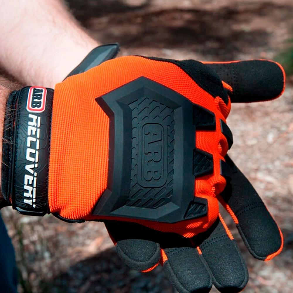 A man is holding a pair of ARB Recovery Gloves GLOVEMX for protection made with orange and black materials.
